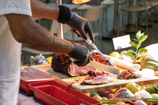 Chef cuts meat dish near roasted veggie platter