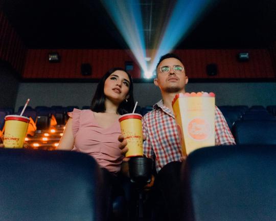 Two people watch a movie with popcorn