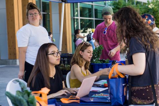 Student sitting at a table talking to another student that is standing