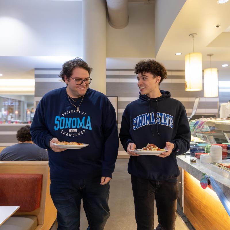 Two students walking in the dining hall with plates full of food