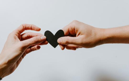 2 hands holding a dark paper heart