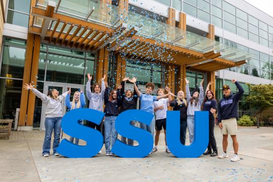 Students cheering with hands up in the air with confetti and large SSU letters in front of them
